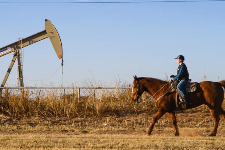 A rider passes by a pumpjack during an evening horseback ride through a residential area in Gardendale, Texas, on Sunday. Photo by Eli Hartman for The Texas Tribune
