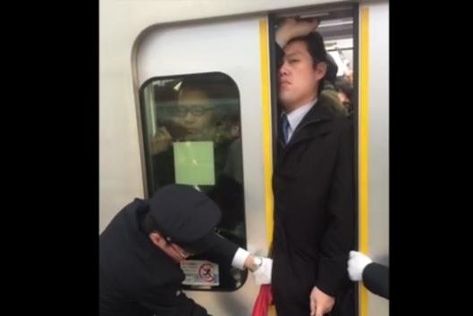 Tokyo subway workers help a commuter cram into an overcrowded train. Screenshot: Storyful