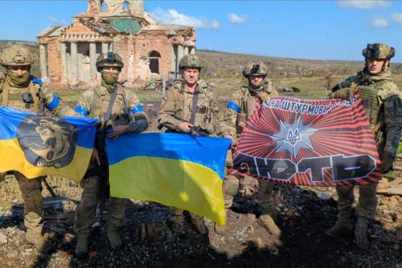 Soldiers pose with the Ukrainian and unit flags in front of a church in the village of Klishchiivka, Donetsk Oblast, on Sunday after recapturing it from Russian forces. Photo courtesy Andriy Yermak/Telegram