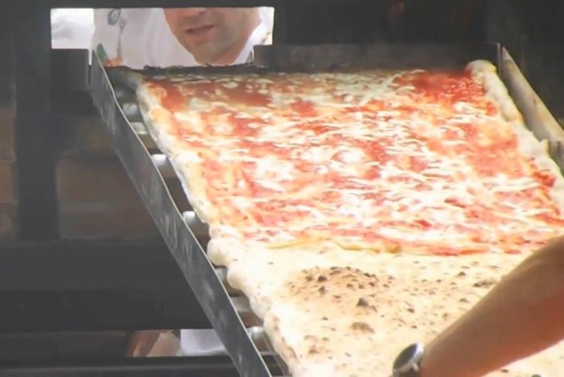 Chefs cook a portion of the Guinness record-breaking 6,082-foot-long pizza. Screenshot: Newsflare