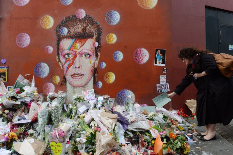 Flowers are piled around a portrait in tribute to British singer David Bowie at his place of birth in Brixton in London on Tuesday. David Bowie died Jan. 10, after an 18-month battle with cancer. Photo by Rune Hellestad/UPI | <a href="/News_Photos/lp/58b1af29001559d8196e514ba1fa2b47/" target="_blank">License Photo</a>