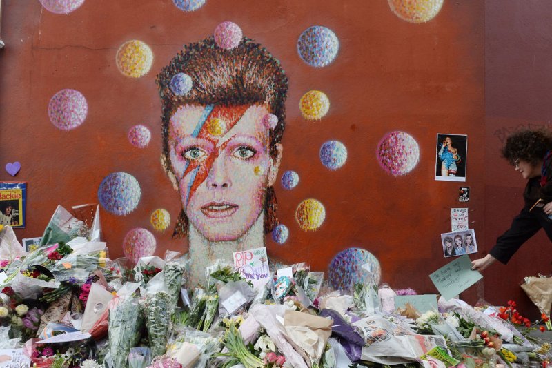 Flowers are piled around a portrait in tribute to British singer David Bowie at his place of birth in Brixton in London on January 12, 2016. David Bowie died January 10, after an 18 month battle with cancer. His ex-wife, Angie Bowie, has left "Celebrity Big Brother" following his death. File Photo by Rune Hellestad/UPI | <a href="/News_Photos/lp/58b1af29001559d8196e514ba1fa2b47/" target="_blank">License Photo</a>