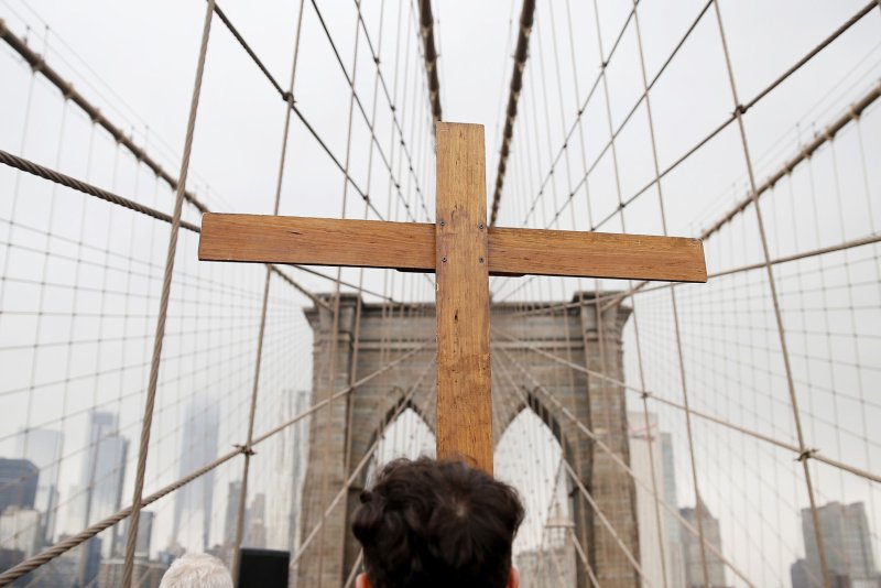 A wooden cross is held and leads the way at the Way of the Cross event that leads a procession over the Brooklyn on March 30, 2018 in New York City. the Catholic Diocese of Rochester has reached a $55 million settlement with survivors of sexual abuse. File Photo by John Angelillo/UPI