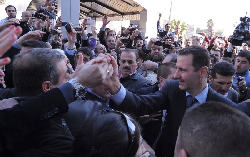 A handout picture released by the Syrian Arab News Agency (SANA) shows Syrian president Bashar al-Assad (R) shaking hands with his supporters upon his arrival to vote for the referendum on a new constitution, at a polling station, in Damascus, Syria, February, 26 2012. Syrians began voting on February 26 on a new constitution that the government says will introduce political pluralism. More than 14,000 polling stations opened nationwide for about 15 million eligible voters. The opposition announced a boycott of the referendum. UPI.