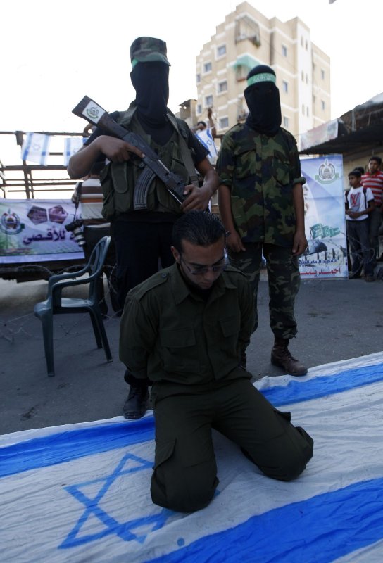 Hamas militants stand next to an Israeli flag and a man acting as captured Israeli soldier Gilad Shalit during a protest on November 1, 2010 in Rafah, southern Gaza Strip, calling for the release of Palestinian prisoners from Israeli jails. UPI/Ismael Mohamad