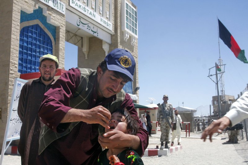 A Pakistani health worker gives the polio vaccine to a child who crossed into Pakistan across the Pakistani-Afghan border at Chaman, Pakistan on May 29, 2013. A guard stands near as security for the polio workers is tight after the attacks on polio teams in Pakistan. UPI/Matiullah Achakzai.