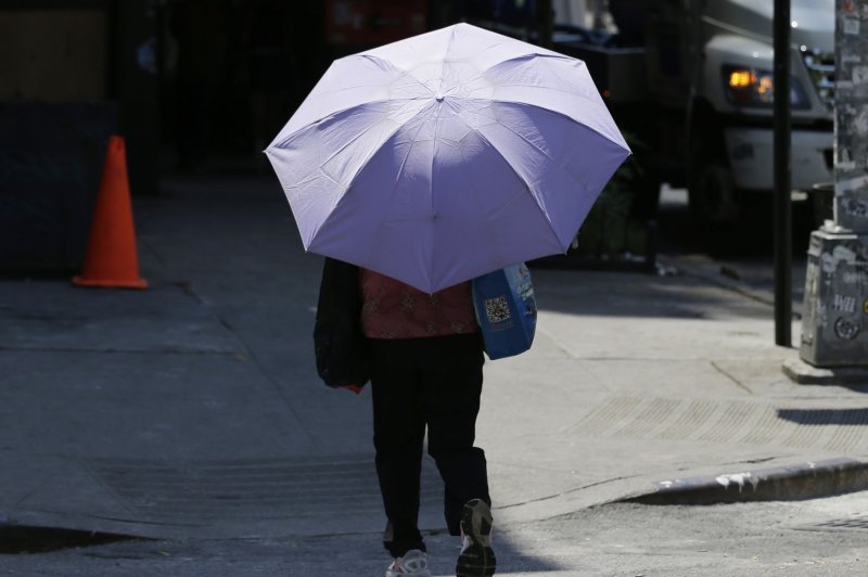 A woman carries an umbrella to shield her from the sun in the East Village of Manhattan in New York City on July 25, 2016. A Chinese firm offering umbrella rentals reported that most umbrellas were stolen. Photo by John Angelillo/UPI