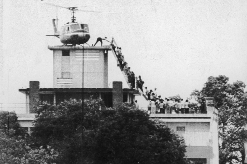 An Air America helicopter crew member helps evacuees up a ladder on the roof of 18 Gia Long St. in Saigon on April 29, 1975, shortly before the city fell to advancing North Vietnamese troops. An erroneous caption once described the helicopter as atop the U.S. Embassy. File Photo by Hugh Van Es/UPI