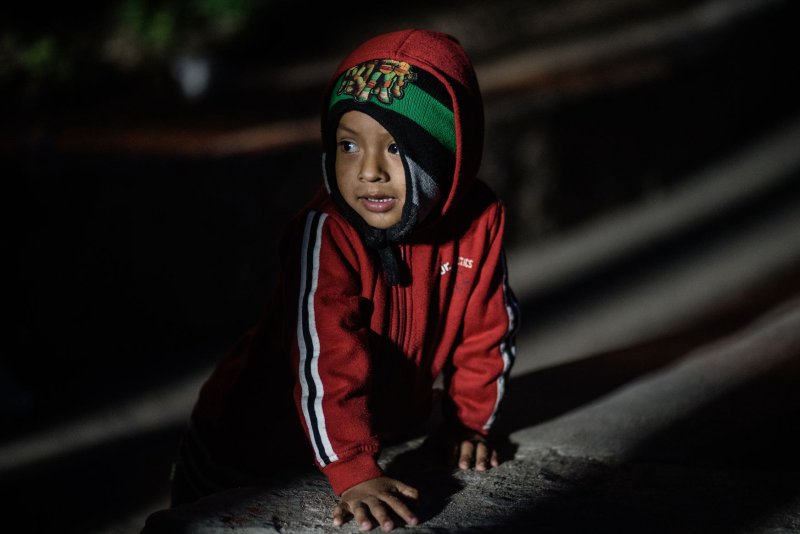 A young child, part of an immigrant caravan in December 2018, looks at the U.S. border fence from Playas de Tijuana, Mexico. Researchers say that children separated from the parents after making it over the border now suffer from PTSD, among other health issues. File Photo by Ariana Drehsler/UPI