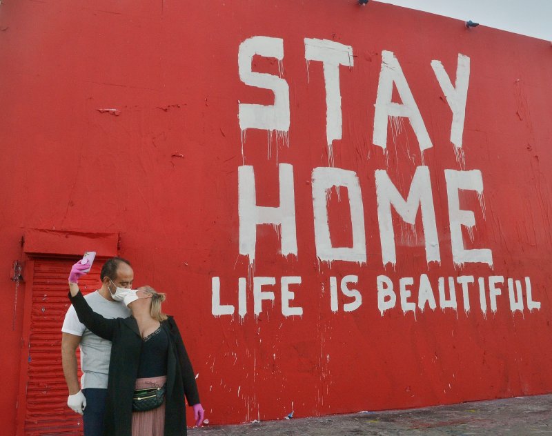 A mural urges residents to stay home as a couple wearing masks kiss while taking a selfie on La Brea Avenue in Los Angeles on Saturday. Some urban artists have been inspired by the coronavirus pandemic. Photo by Jim Ruymen/UPI