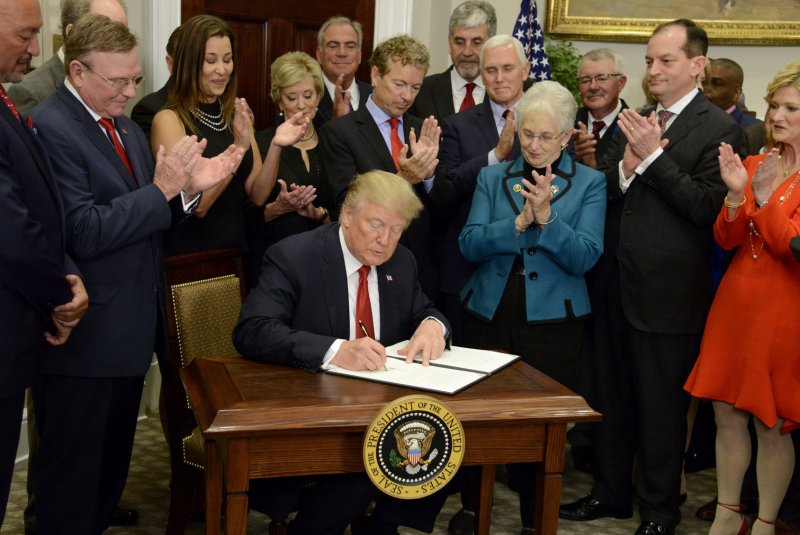 President Donald Trump, surrounded by Republican lawmakers and members of his Cabinet, signs an executive order Thursday to allow health insurance companies to sell cheaper, less beneficial plans to younger Americans. Photo by Mike Theiler/UPI