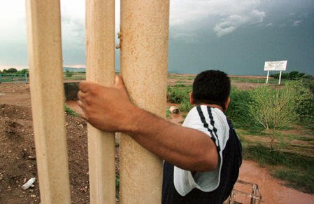 A "coyote" or guide for illegal aliens hangs onto the end of the fence marking the US-Mexico border. Jack Kurtz/File/ UPI