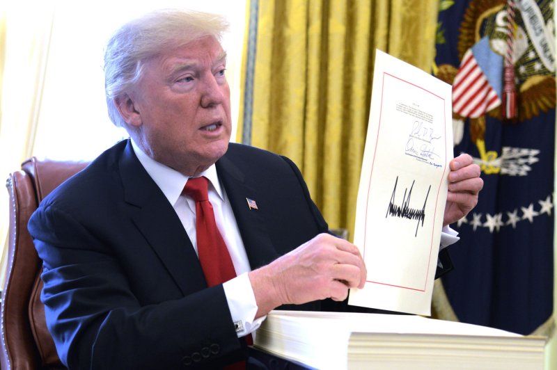 President Donald Trump displays his signature after signing the $1.5 trillion tax cut bill, stacked on his desk, in the Oval Office on Friday prior to his departure to Mar-a-Lago, Florida for the holidays. Photo by Mike Theiler/UPI