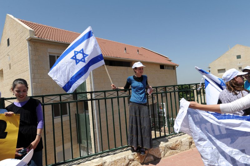 An Israeli settler holds the national flag in front of a house built on private Palestinian land in the Ulpana settlement outpost in the West Bank, June 4. The settlers are marched from the Ulpana settlement outpost to Jerusalem to demonstrate against Israeli Prime Minister Binyamin Netanyahu's plan to relocate five homes built on private Palestinian land following a order by the Israeli Supreme Court. UPI/Debbie Hill