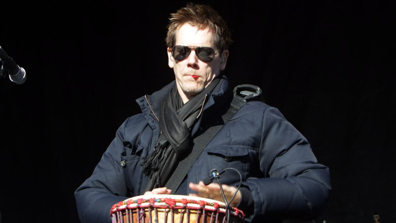 With a guitar pick in his mouth, actor Kevin Bacon plays the drum as part of the Bacon Brothers Band during the Pet Parade in St. Louis on February 3, 2013. (File/UPI/Bill Greenblatt)