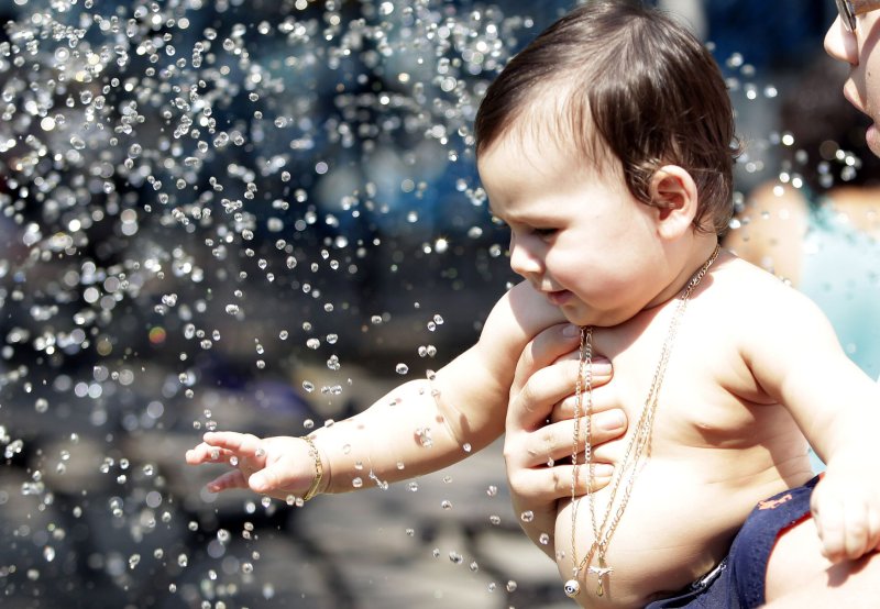 A baby reaches out to touch water at a fountain with temperatures around 100 degrees in the East Village of New York City on June 21, 2012. UPI/John Angelillo