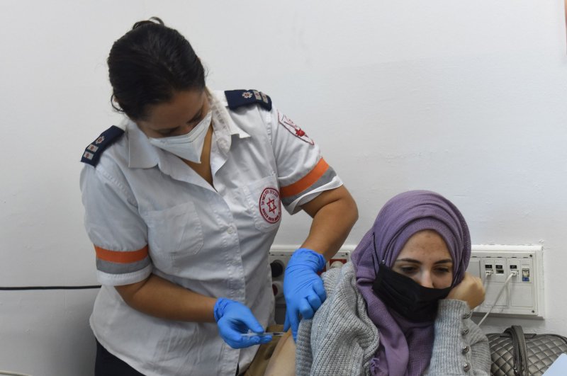 A paramedic with Magen David Adom, Israel's National Emergency Organization, administers the Pfizer-Biotech coronavirus vaccine to a Palestinian woman at the Qalandiya Checkpoint Tuesday. Photo by Debbie Hill/UPI | <a href="/News_Photos/lp/0a936bceb64f083cc2fec6873c519cc7/" target="_blank">License Photo</a>