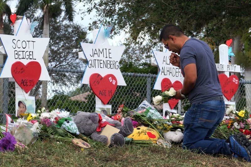A mourner kneels at markers commemorating the 17 students, teachers and staff who died in the mass shooting at Marjory Stoneman Douglas High School in Parkland, Fla., days afterward. File Photo by Gary Rothstein/UPI