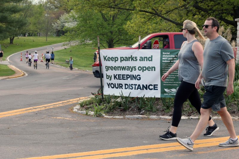 A couple walk around Tillis Park in Ladue, Mo., with new signage, hours after the park reopened, on April 28. A stagnant weather pattern has set up across the central and eastern United States, sparking daily rounds of showers and heavy thunderstorms into the start of July. Photo by Bill Greenblatt/UPI