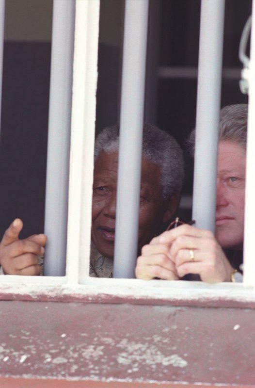 South African President Nelson Mandela (L) and U.S. President Bill Clinton on March 27, 1998, view Cell Block B at Robben Island, South Africa, where Mandela was imprisoned. On March 26, 1998, Clinton became the first U.S. president to visit South Africa. File Photo courtesy of the White House/Wikimedia