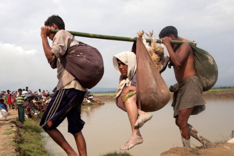 Rohingya Muslims assists an elderly woman as they enter Bangladesh near the Bangladesh-Myanmar border earlier this month. A boat carrying 40 refugees capsized off the Bangladesh coast, killing 14 people. Photo by EPA-EFE/STR