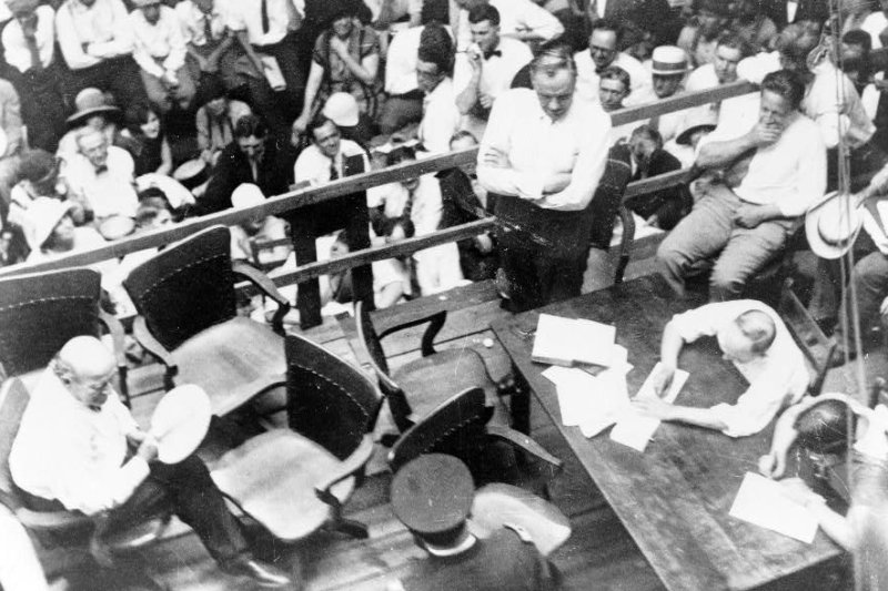 Photograph shows William Jennings Bryan (seated, left, with fan) and Clarence Darrow (standing, center, with arms folded) at an outdoor courtroom during the Scopes Trial (Tennessee v. Scopes) in Dayton, Tenn., in July 1925. UPI File Photo