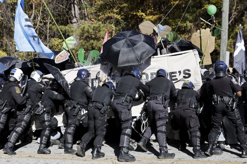 epaselect epa10973479 Police officers in riot gear confront demonstrators carrying a banner and protesting at the construction site of the Atlanta Public Safety Training Center, known as Cop City, in the South River Forest area near Atlanta, Georgia, USA, 13 November 2023. The group is opposed to the construction of the combined training facility for the Atlanta Police Department and Atlanta Fire Rescue Department. An environmental activist has been killed and dozens of protesters have been charged with state RICO charges since the movement began. EPA-EFE/ERIK S. LESSER