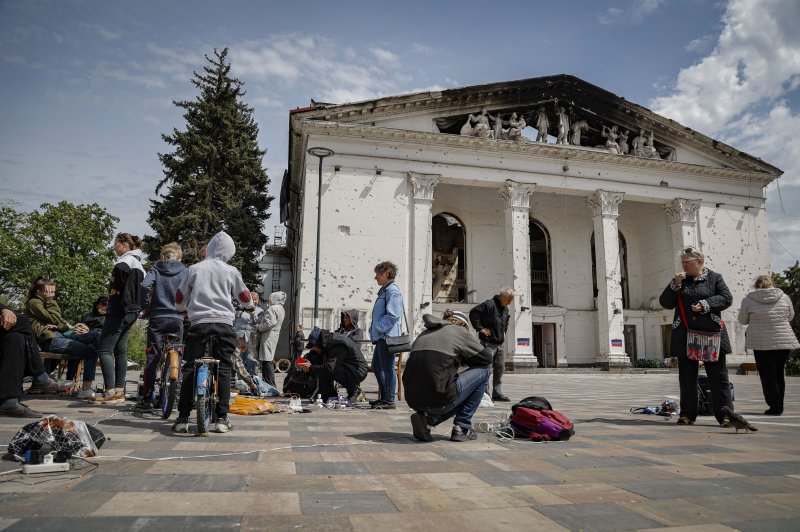 People charge their cellphones outside the destroyed theater in Mariupol, Ukraine, on May 21. An investigation by Amnesty International determined Russia intentionally targeted civilians taking refuge inside the building in March. File Photo by Alessandro Guerra/EPA-EFE