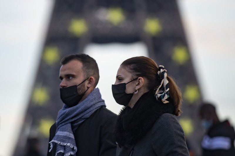 Pedestrians wear face masks walk near the Eiffel Tower iluminated in the colors of the European Union flag to mark France's presidency of the EU, in central Paris on Sunday. Pjoto by Ian Langsdon/EPA-EFE