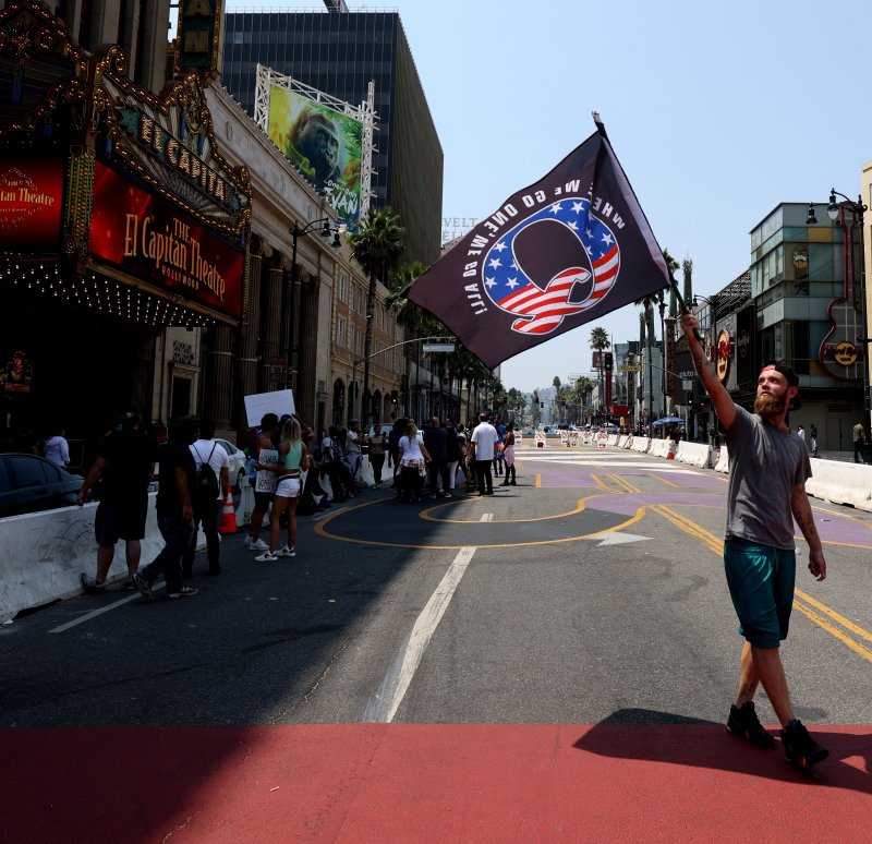 A man holds a QAnon conspiracy flag while walking over the All Black Lives Matter mural in Hollywood, Calif., on August 22. The QAnon conspiracy, without evidence, accuses Hollywood actors of engaging in crimes against children. File Photo by Christian Monterrosa/EPA-EFE