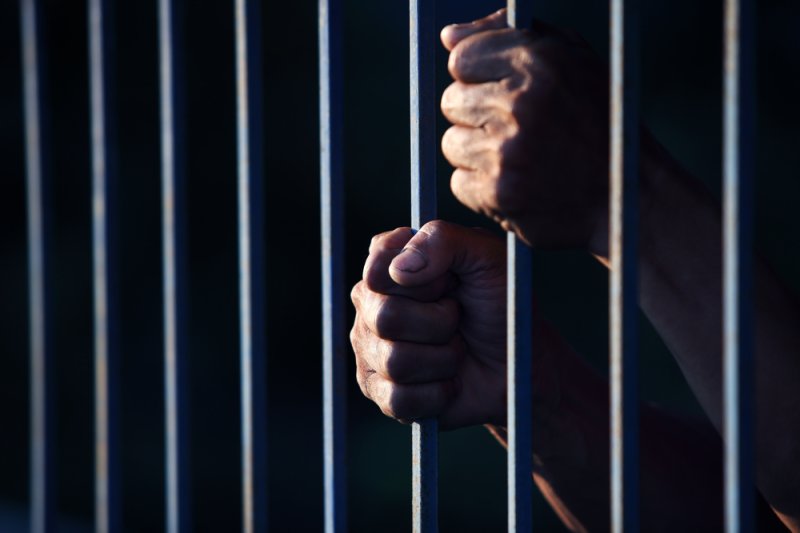 A man in jail grasps the bars of his prison cell. (UPI/Shutterstock/sakhorn)